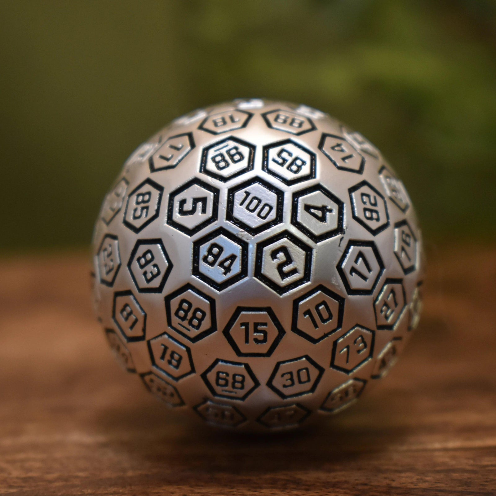 A large, silver, metal D100 dice with black engravings on a hexagonal pattern.