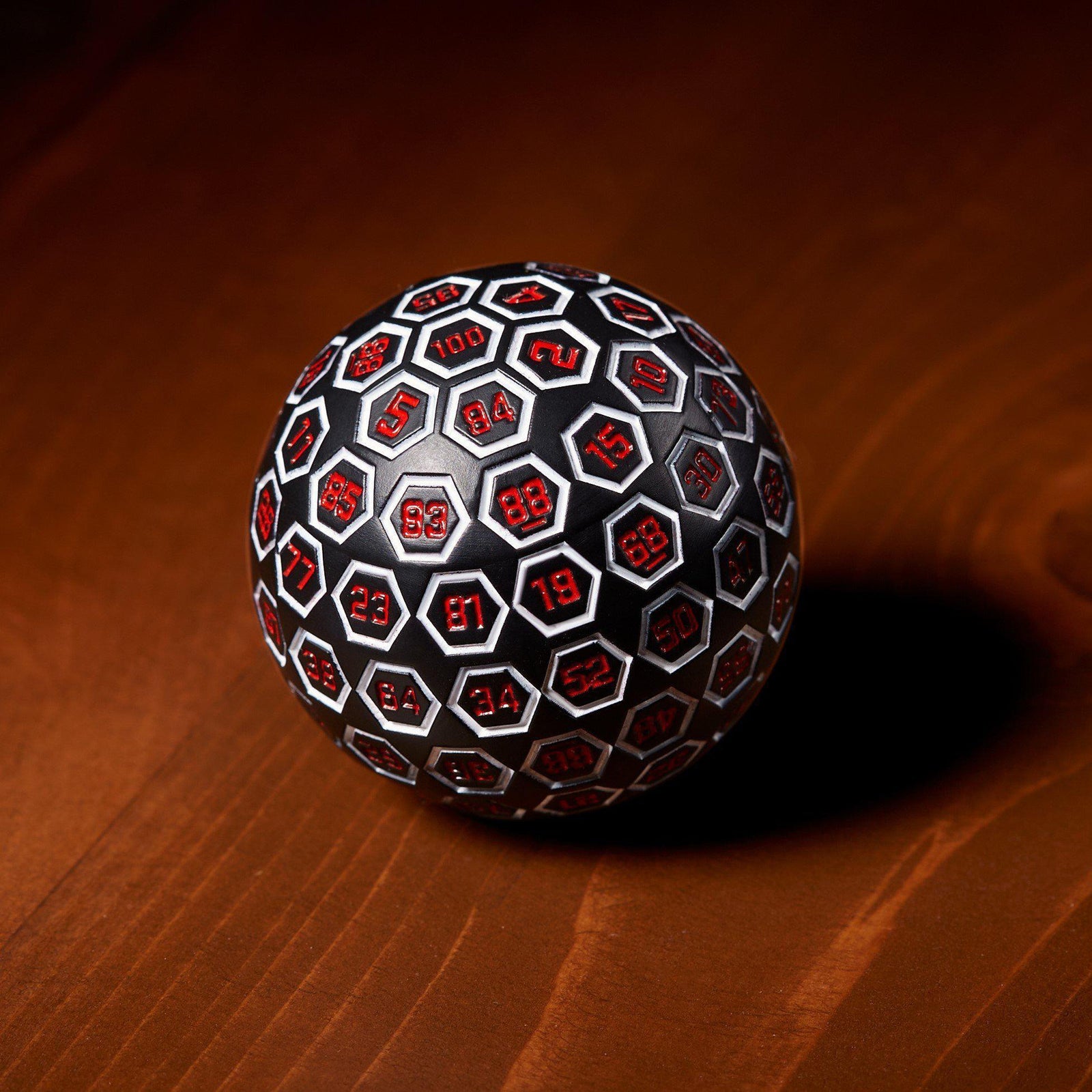 A large white, red, and black metal D100 dice on a wooden surface.