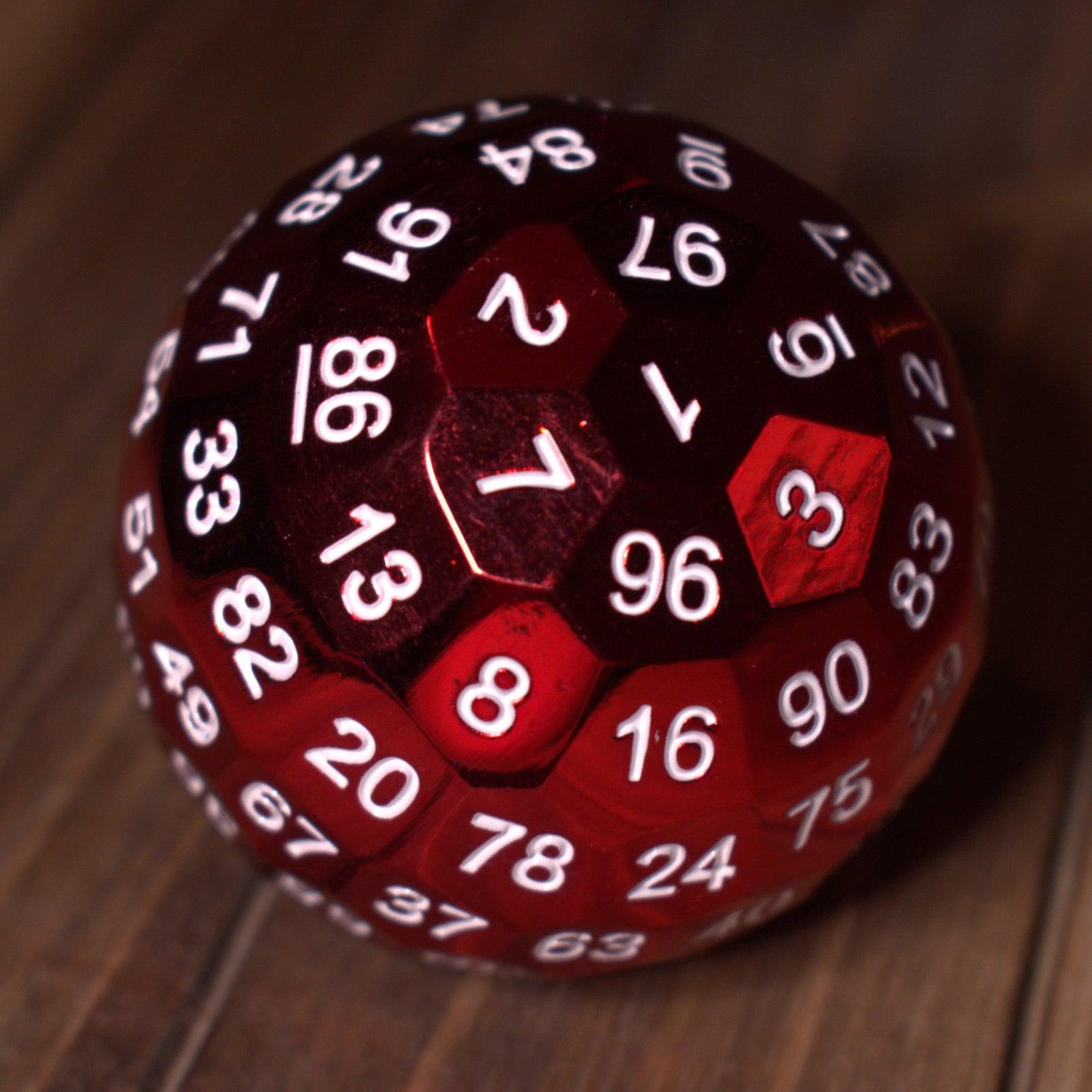 A large red metal d100 dice with white numbers on a wooden surface.