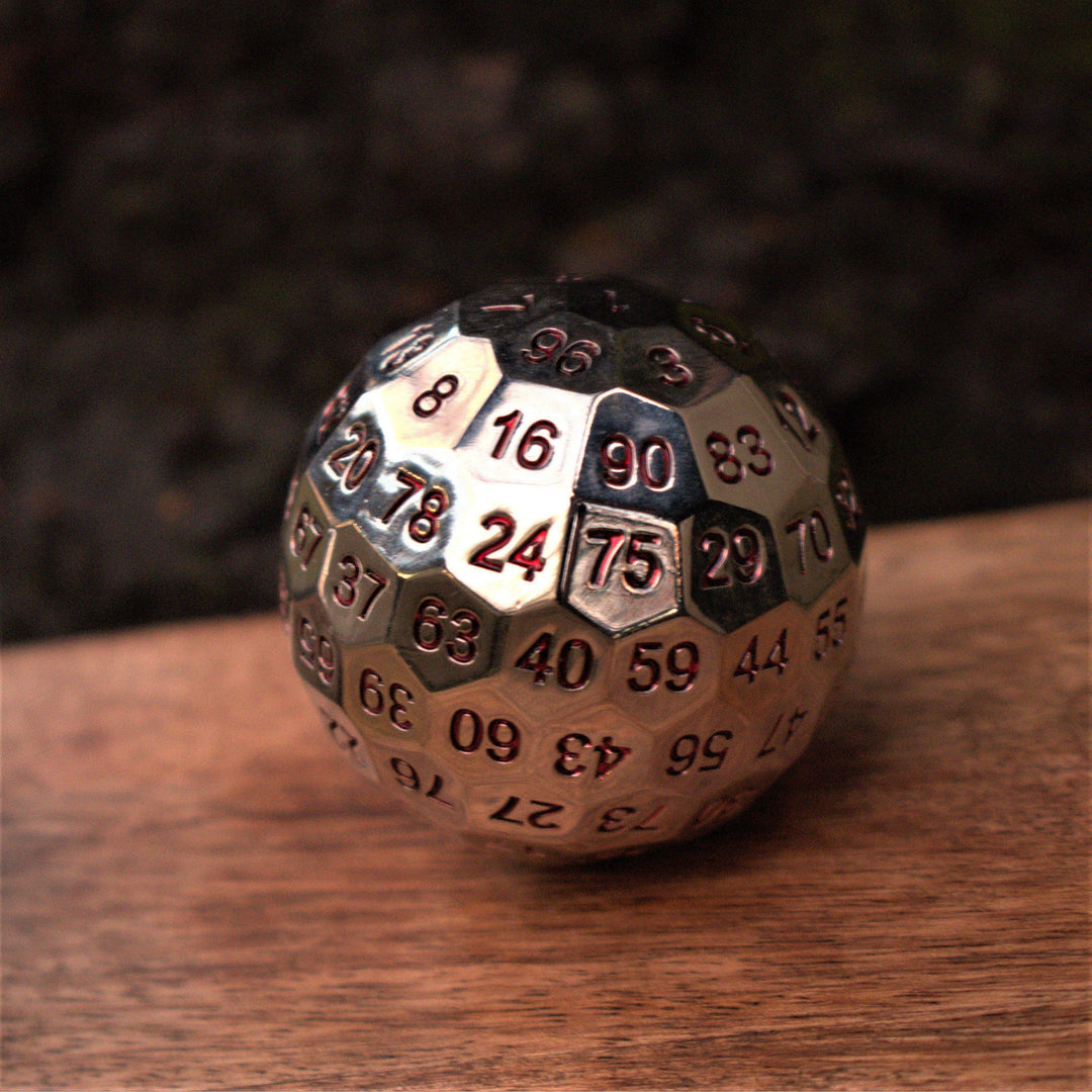 A large silver metal d100 dice with red engraved numbers, resting on a wooden surface for wargaming tabletop gaming board games