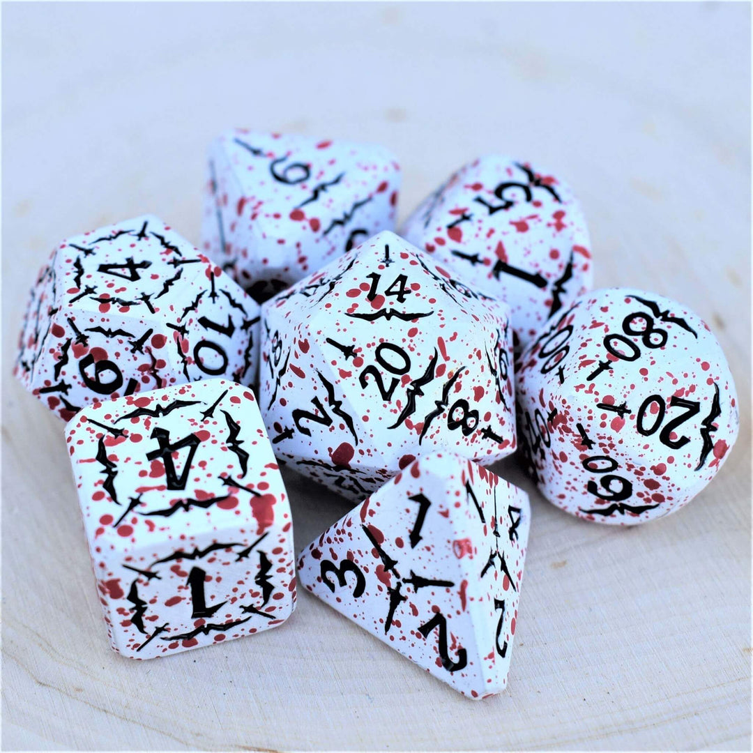 A collection of metal dice with engraved numbers, featuring a white base with black and red speckles, including specific dice shapes such as a d4, d6, d8, d10, d12, and d20.