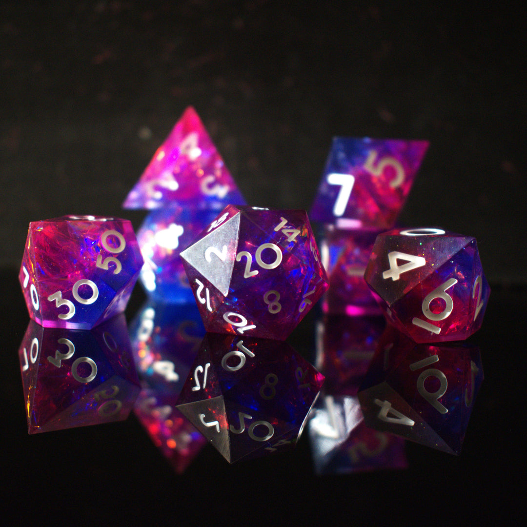 A set of sharp-edged resin dice in pink and purple colors with engraved white numbers, reflecting on a shiny surface.
