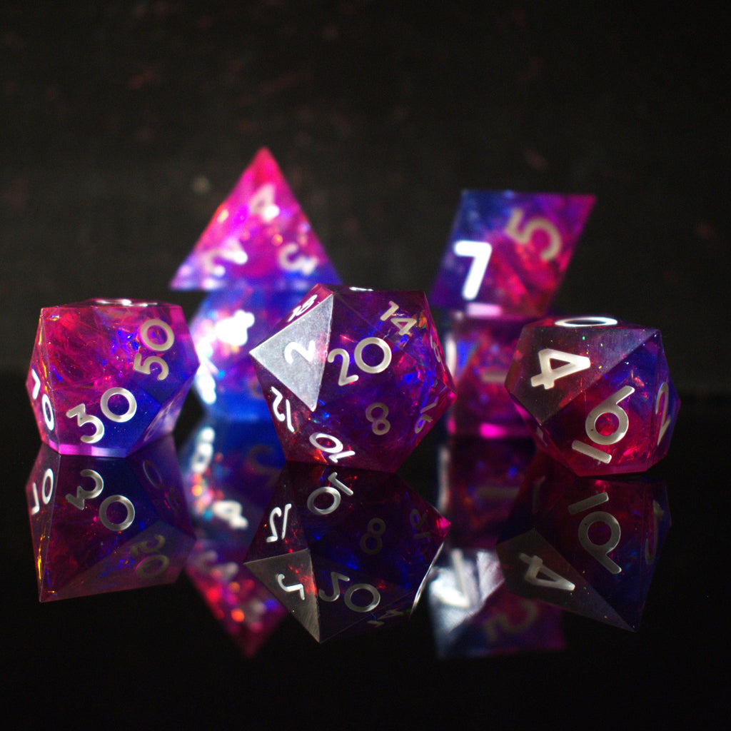 A set of sharp-edged resin dice in pink and purple colors with engraved white numbers, reflecting on a shiny surface.