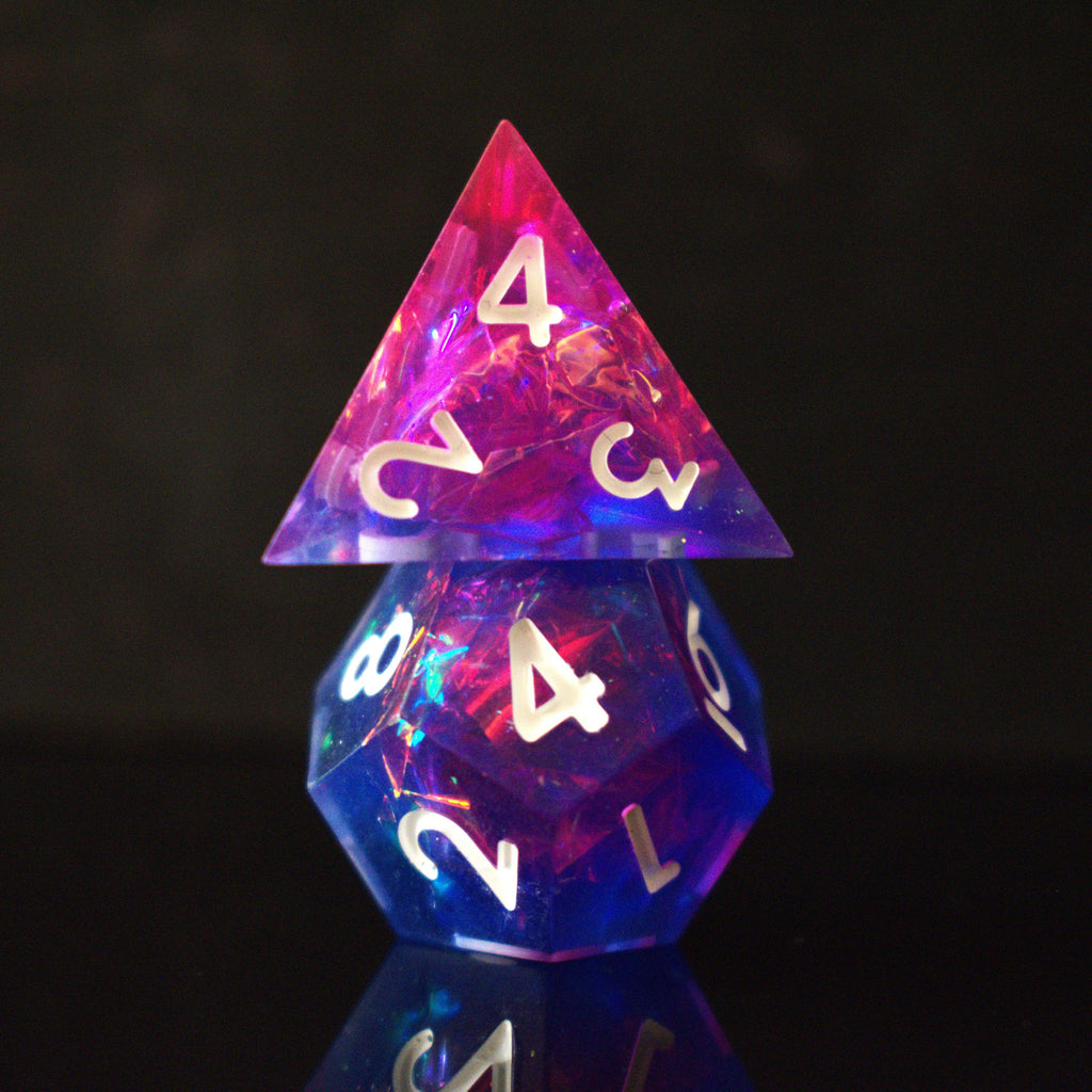 A set of sharp-edged resin dice in pink and purple colors with engraved white numbers, reflecting on a shiny surface.