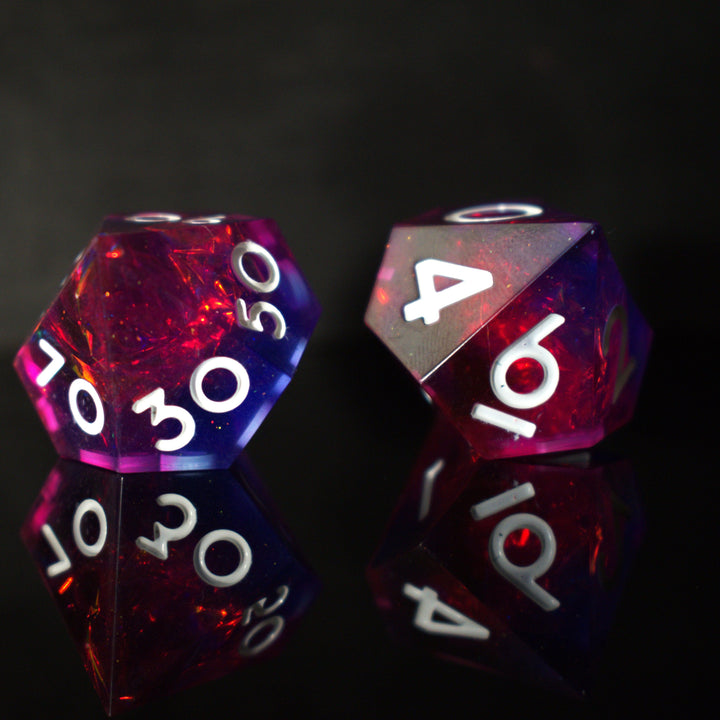 A set of sharp-edged resin dice in pink and purple colors with engraved white numbers, reflecting on a shiny surface.