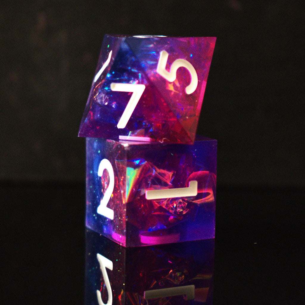 A set of sharp-edged resin dice in pink and purple colors with engraved white numbers, reflecting on a shiny surface.