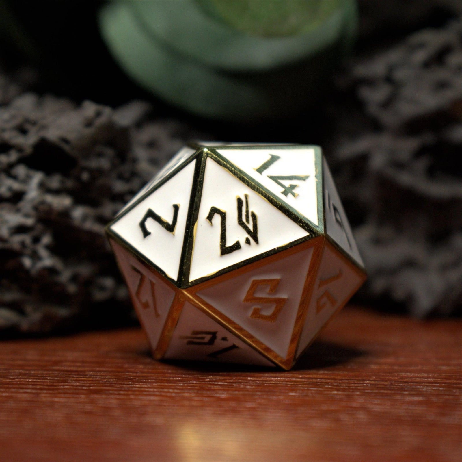 A single 35mm white and gold metal D20 dice with embossed numbers placed on a reflective surface.