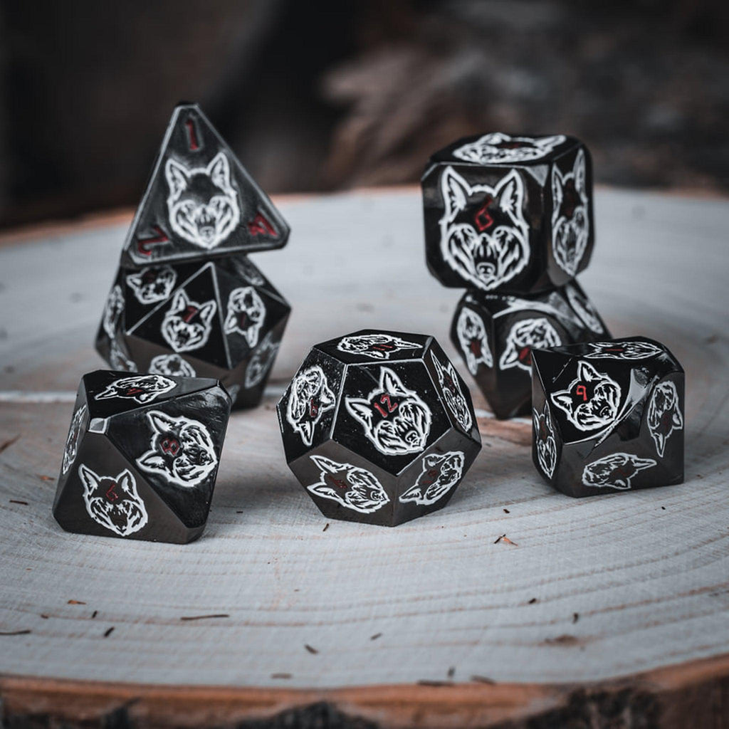 A set of black metal dice with white wolf head designs on each face and red small numbers on a wooden surface