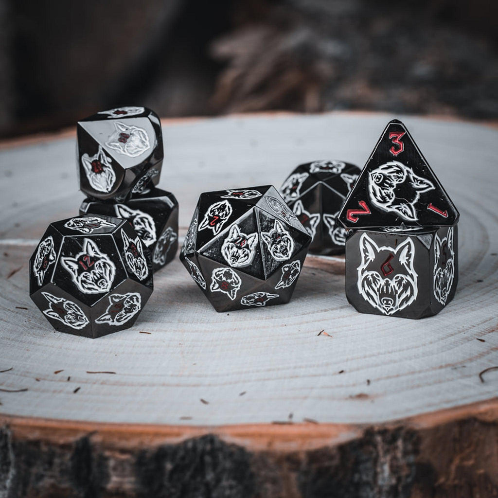 A set of black metal dice with white wolf head designs on each face and red small numbers on a wooden surface
