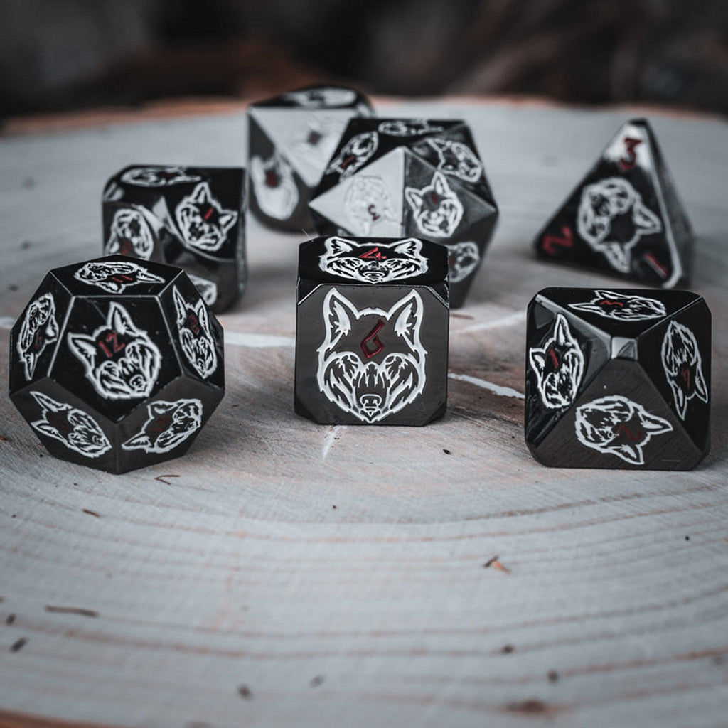 A set of black metal dice with white wolf head designs on each face and red small numbers on a wooden surface