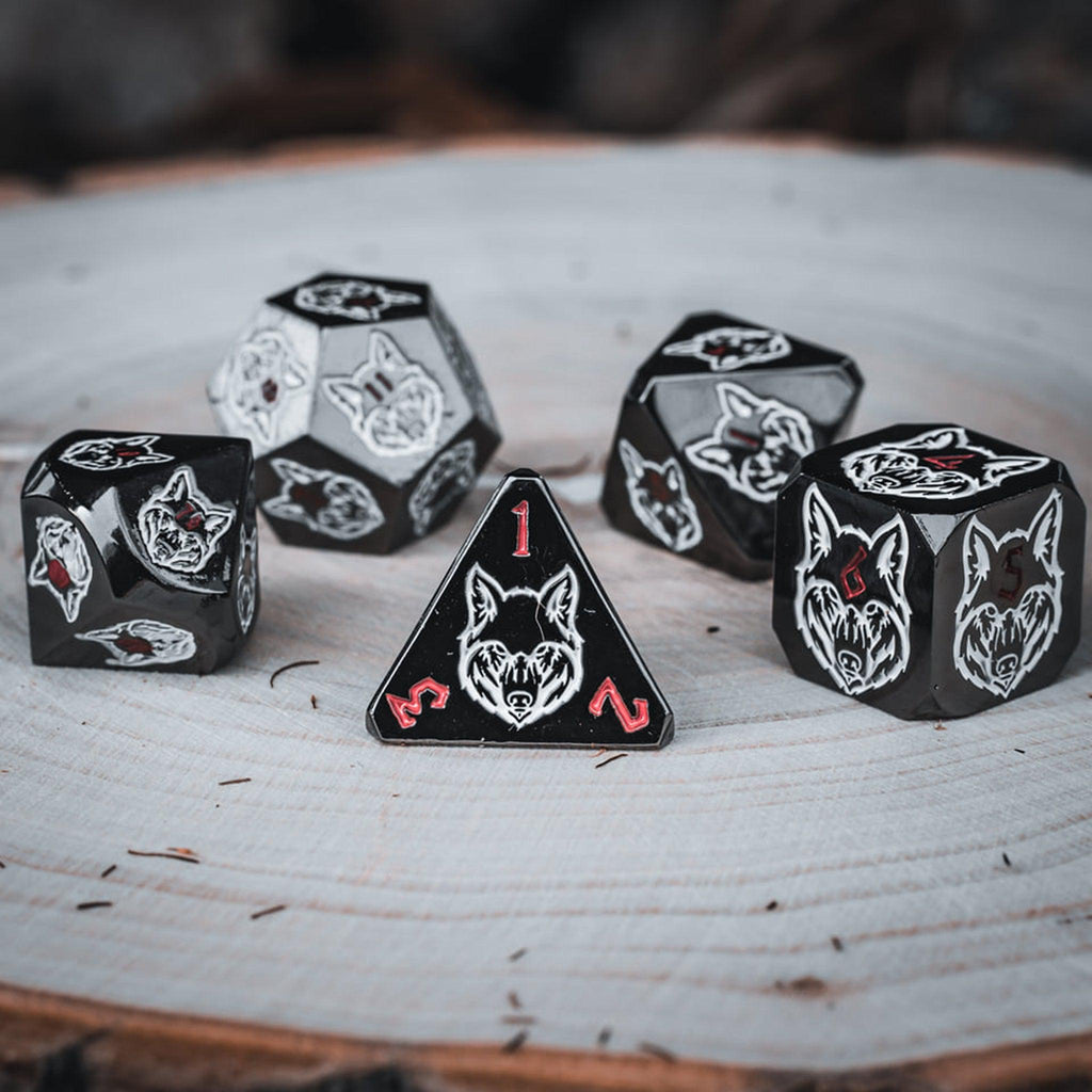 A set of black metal dice with white wolf head designs on each face and red small numbers on a wooden surface