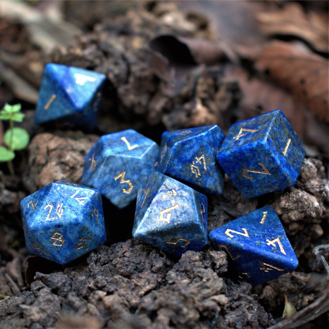 A close-up of a blue lapis lazuli stone ttrpg dice set with engraved numbers, placed on a wooden surface.